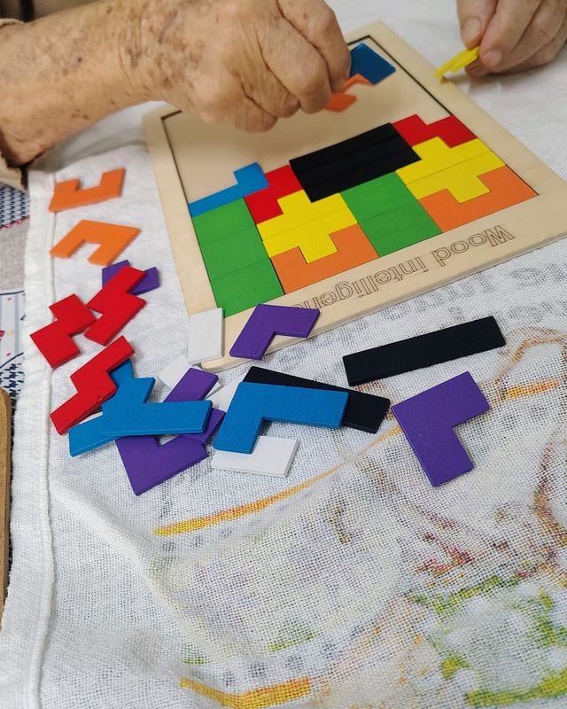 Mãos de uma pessoa idosa montando um quebra-cabeça de peças coloridas