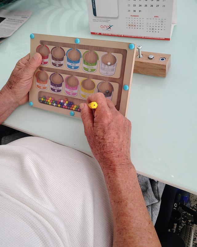 Mãos de uma pessoa idosa movendo peças em um tabuleiro de cores